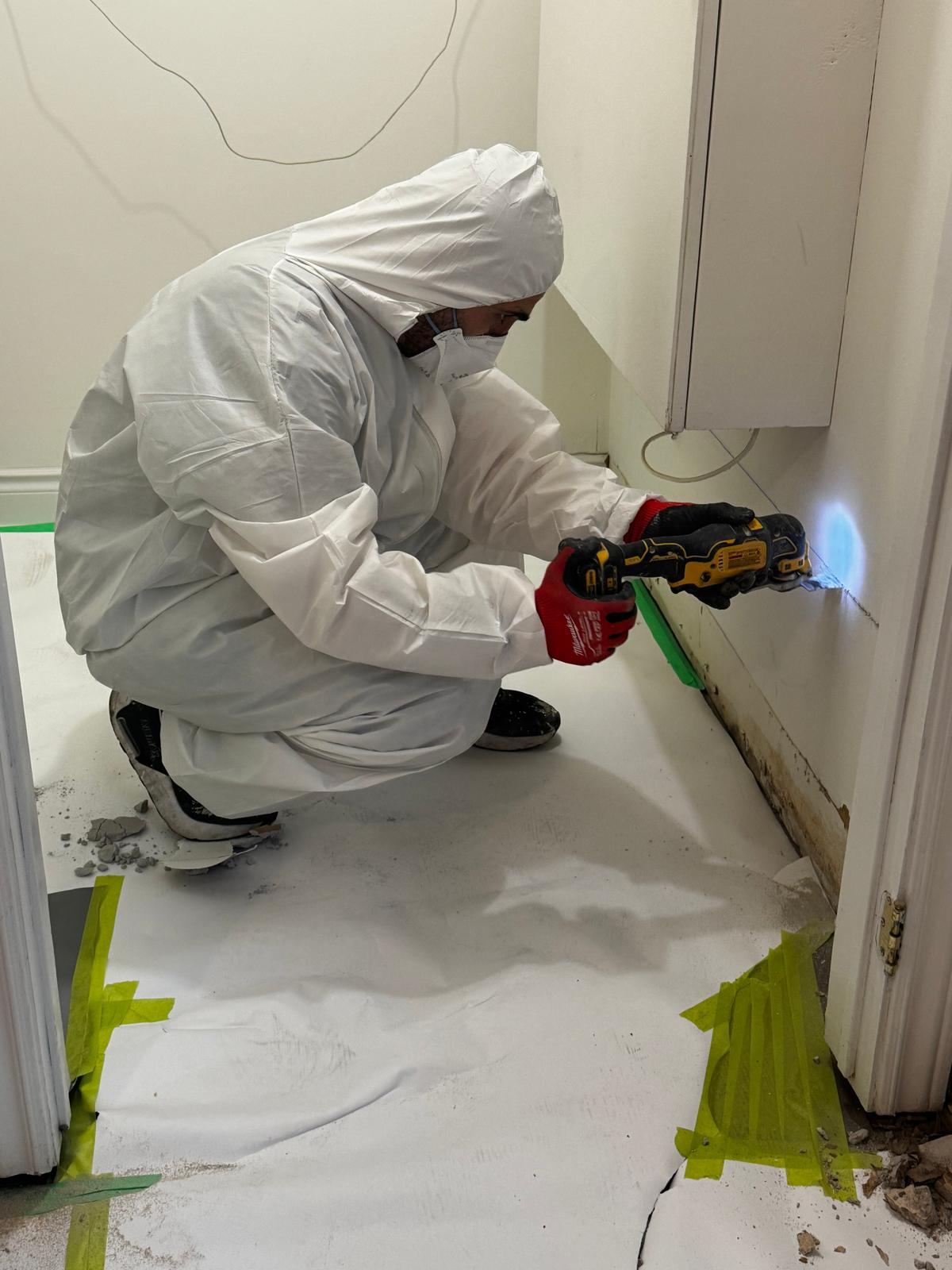 Safesite technician in a protective suit cutting out water-damaged drywall