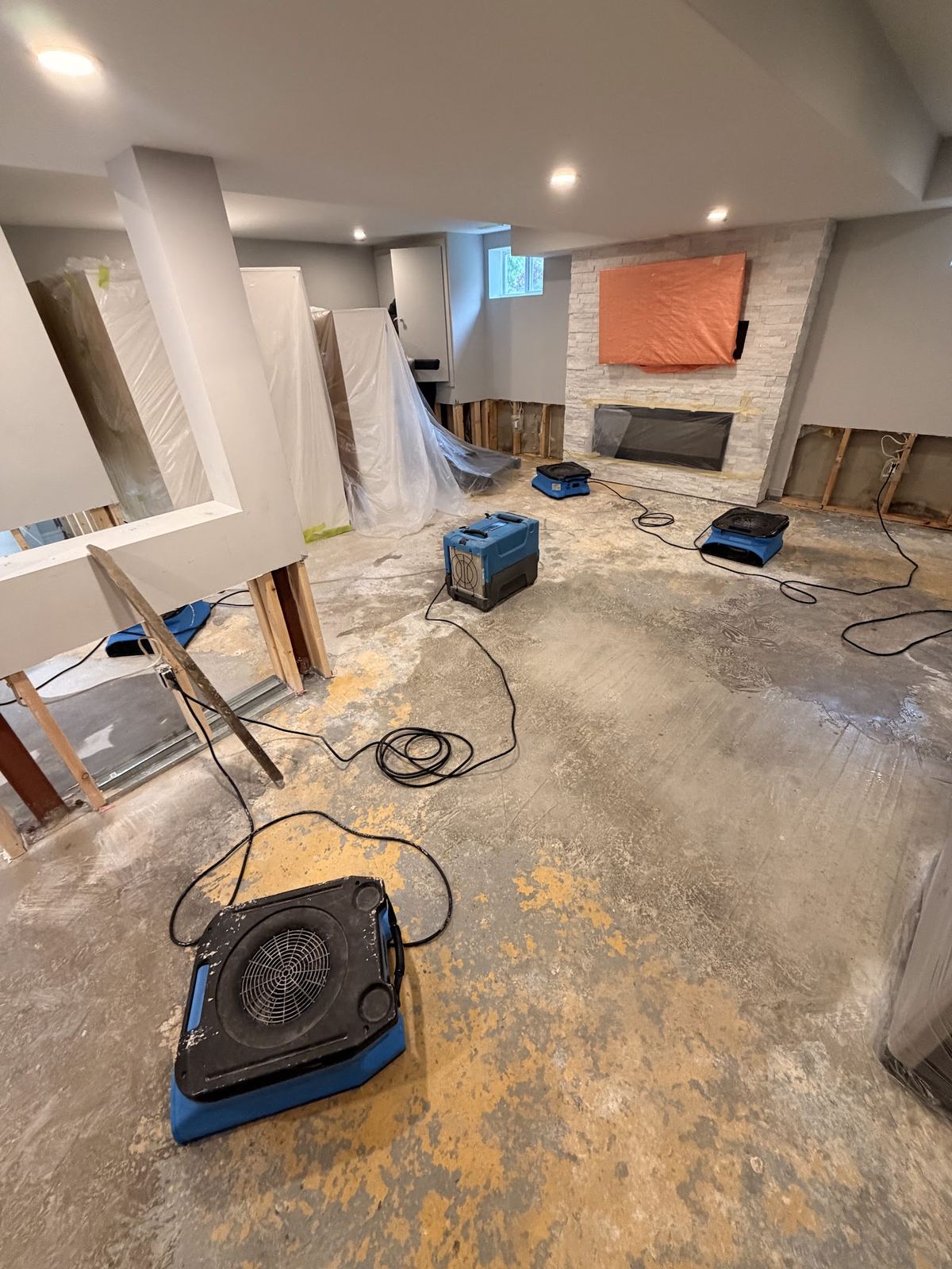 Air movers and dehumidifiers drying a flooded basement in Toronto after the wet drywall was cut out